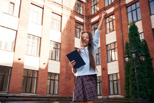 Cheerful, ,celebrating ,success. School girl in uniform is outdoors near the building photo