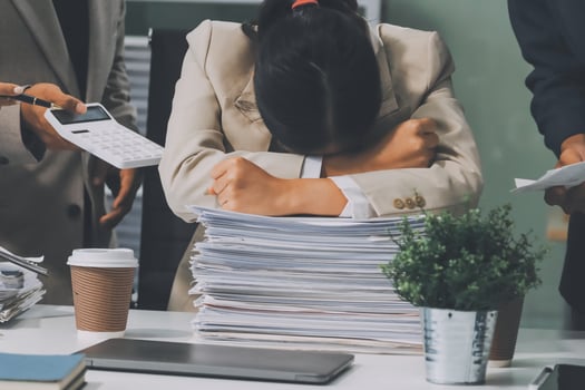 A woman is holding her head in her hands while sitting at a desk with a pile of papers photo