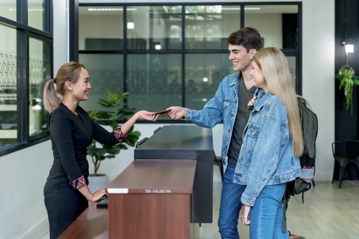 Young couple handing passport to hotel receptionist at front desk during check-in, showing hospitality, travel documentation, and customer service photo