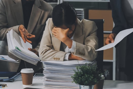 A woman is holding her head in her hands while sitting at a desk with other people photo
