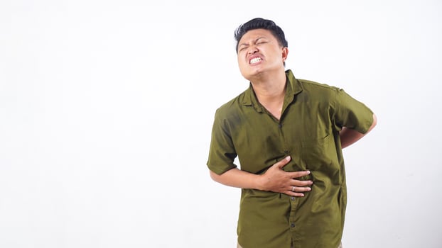 Young Asian male experiencing severe stomach cramps and discomfort isolated on white background photo