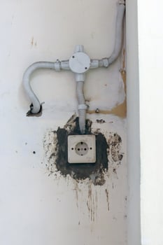 Old wall power outlet with visible dirt and exposed wiring, perfect for illustrating neglected electrical infrastructure, decay, or maintenance issues photo