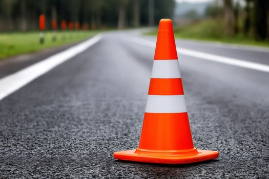 Orange traffic cone standing on asphalt road leading to forest photo