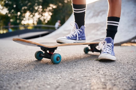 Standing on skateboard on one leg. Close up view of a young girl legs in blue shoes, photo