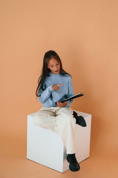 With tablet in hands. Sitting, on cube. Cute young girl is in the studio against background photo
