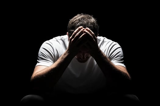 A man sitting in the dark with his hands on his head photo