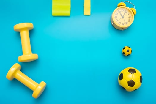 Yellow sports items, dumbbells, balls, elastic bands for sports, alarm clock, on a blue background photo