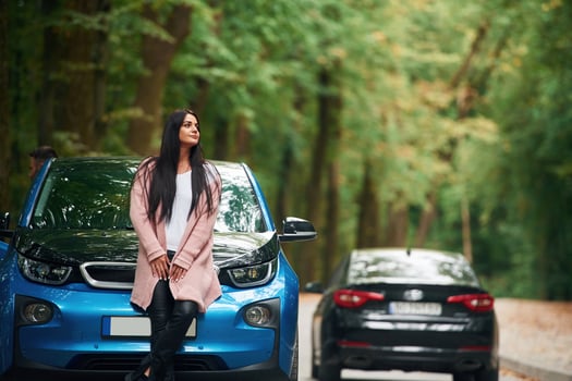 Black automobile, behind. Cheerful ,beautiful woman is near blue car outdoors photo