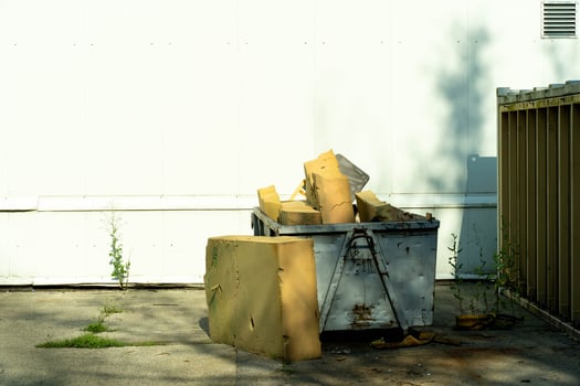 Waste Container Filled with Large Yellow Foam Pieces Near White Wall photo