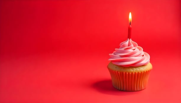A beautifully decorated cupcake with pink frosting and a lit candle on a red background. photo