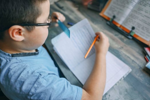 boy in blue shirt using ruler and pencil while doing homework, close up of child writing in notebook at wooden desk with textbook photo