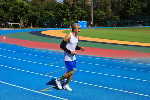 Senior Asian athlete is practicing his running in the professional blue track for professional exercise, sport training workout and healthy for longevity concept photo