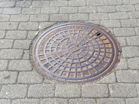 Round metal manhole cover on cobblestone street photo