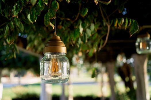 Jar lamp hangs from the ceiling of a pergola entwined with green branches in the garden photo