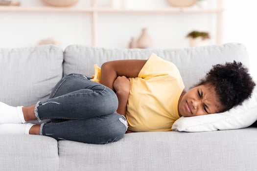 Stomachache. Black Teen Girl Suffering From Abdominal Pain Touching Aching Stomach Lying On Sofa At Home. photo