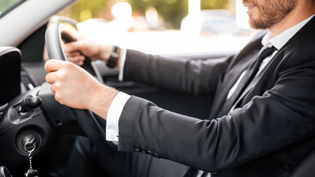 Unrecognizable businessman in black suit holding hands on steering wheel, driving luxury car. Cropped of manager or entrepreneur going to office or to business meeting, enjoying driving photo