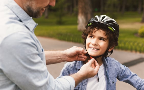 Safety First. Closeup of father putting protection helmet on his little son at park, outdoor shot photo
