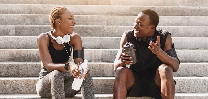 Sporty african american couple resting on steps after training outdoors, drinking water and chatting, free space photo