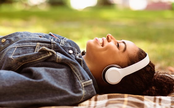 Weekend Relaxation. Happy Black Girl Listening To Music In Headphones Lying On Plaid Relaxing In Park Outside photo