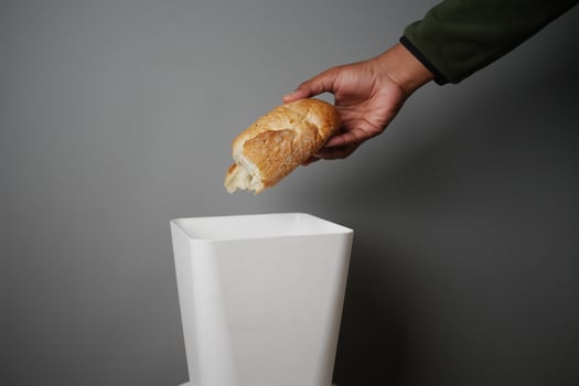 Hand discarding bread into a trash bin in a minimalistic setting photo