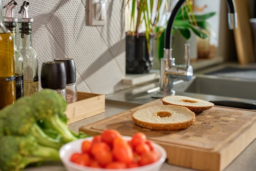 Sliced bagel on wooden cutting board with cherry tomatoes, broccoli and kitchen tools in background. Preparation of healthy breakfast or snack in kitchen photo