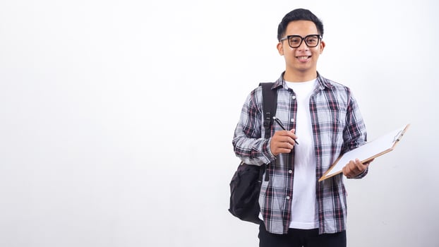 Young Asian male college student with a backpack holding wooden clipboard and pen isolated on white background photo