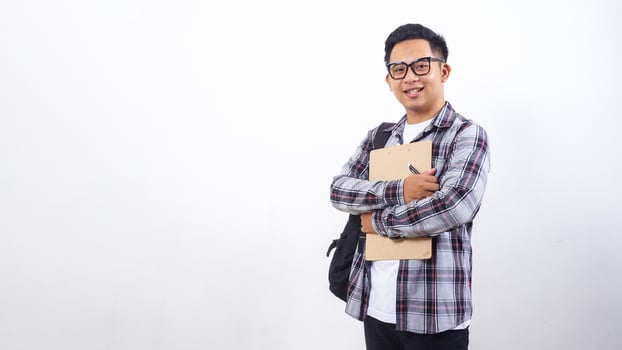 Young Asian male college student with a backpack holding wooden clipboard and pen in front his chest isolated on white background photo
