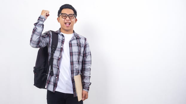 Happy young Asian male college student with a backpack holding clipboard isolated on white background photo