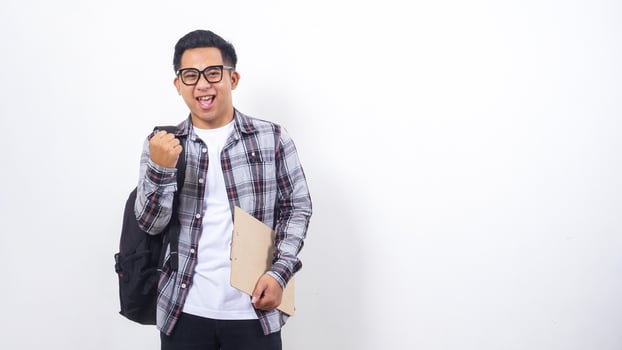 Excited young Asian male college student with a backpack holding clipboard isolated on white background photo