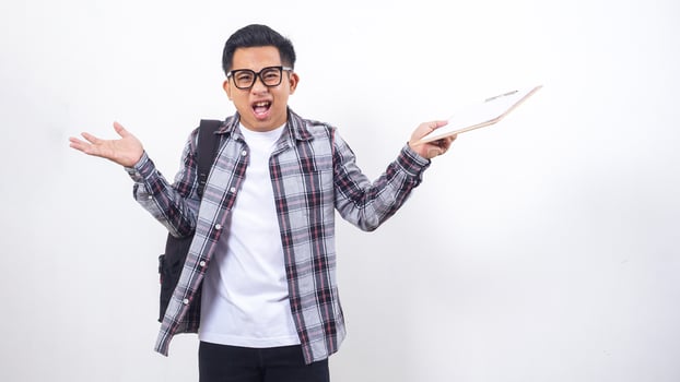 Stressed young Asian male college student with a backpack holding clipboard isolated on white background photo