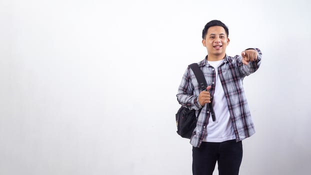 Handsome young Asian male college student with a backpack and showing his finger pointing to camera isolated on white background photo