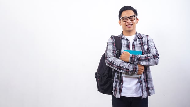Handsome young Asian male university student with a backpack holding books in front of his chest standing isolated on white background photo