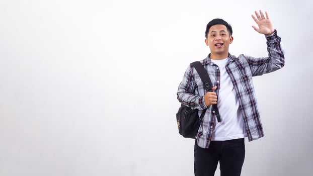 Handsome young Asian male college student with a backpack and showing gesture of greeting isolated on white background photo