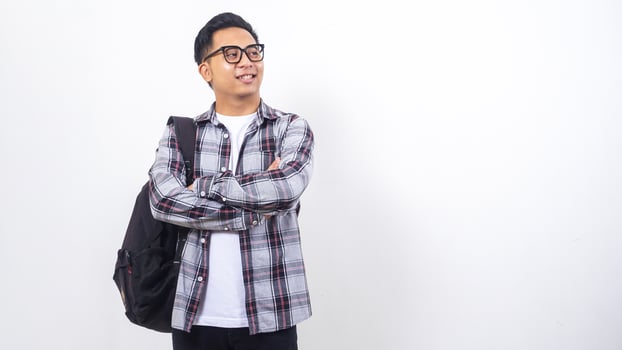 Handsome young Asian male college student with a backpack crossing his arms in front of his chest and looking away isolated on white background photo