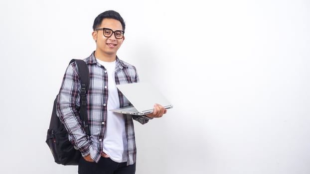 Smiling young Asian male college student with a backpack and holding open laptop with casual pose isolated on white background photo