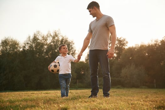 Walking,, and holding soccer ball. Father and little son are playing and having fun outdoors photo