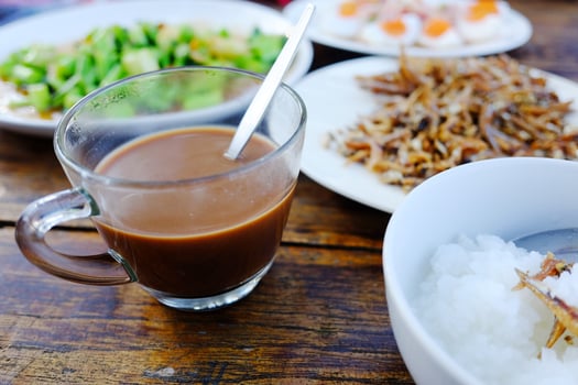 A glass cup of hot coffee with Thai food and boiled rice in white bowl on wooden table. Breakfast in the morning of Thailand photo
