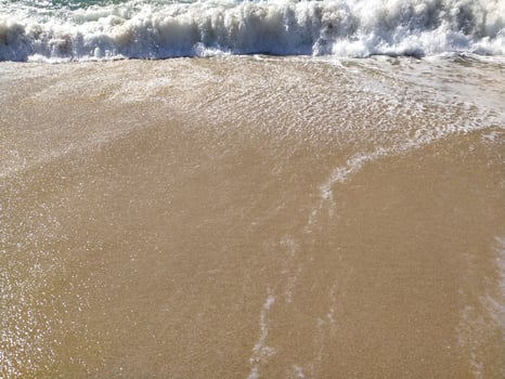 Gentle waves rolling beach at sunrise, creating bubbles and a shimmering surface photo