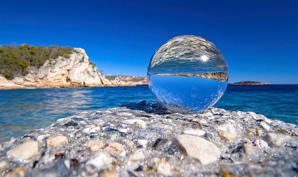 A clear glass ball sitting on a rock near the ocean photo