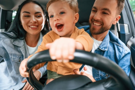 Boy is trying to ride. Family of father, mother and little son are sitting in the modern car. photo