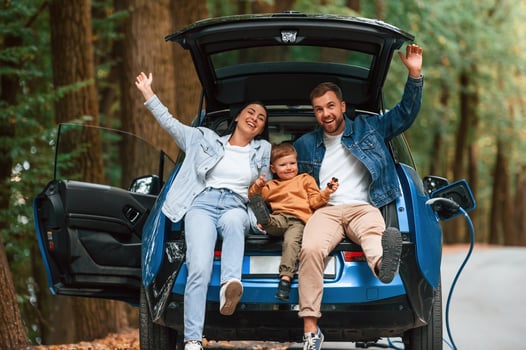 Sitting, on the back, of a vehicle. Mother, father and little son are waiting for electric car to charge outdoors photo