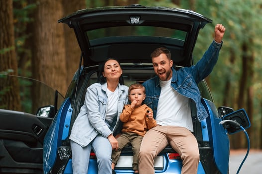 Sitting ,on ,the back of a vehicle. Mother, father and little son are waiting for electric car to charge outdoors photo