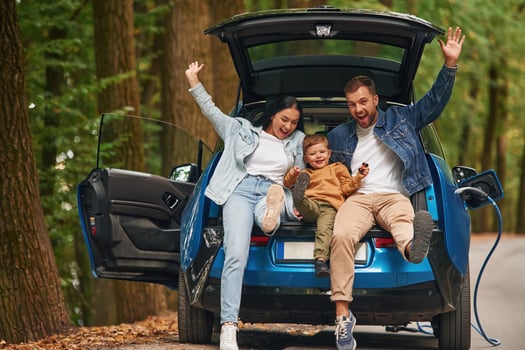 Sitting on the ,back, of a vehicle. Mother, father and little son are waiting for electric car to charge outdoors photo
