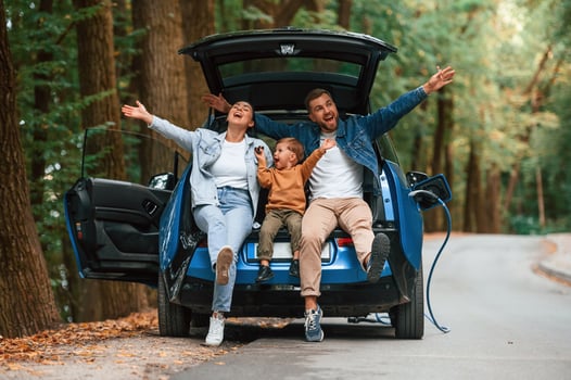 Sitting on the, back of a vehicle. Mother, father and little son are waiting for electric car to charge outdoors photo