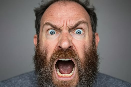 A man with a beard and a blue shirt is making an angry face photo