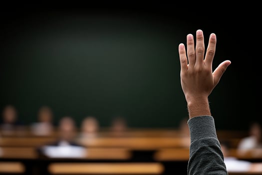 A hand raised in front of a classroom photo
