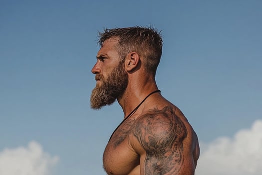 A man with a beard and tattoos standing on the beach photo