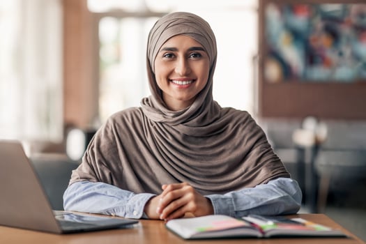 Smiling arab girl looking for job online, sitting at cafe and using laptop, copy space photo