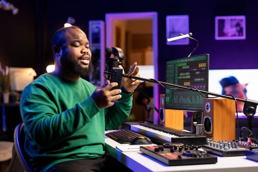 Talented young artist performing an acoustic version of his new song, reading the lyrics on his smartphone. Professional musician producing a new track, recording audio files on microphone. photo