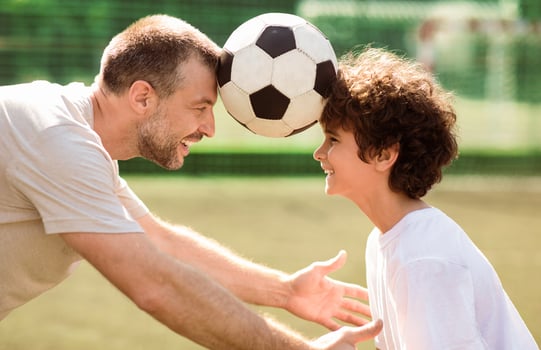 Side view portrait of mature father with his little son playing soccer on football pitch, holding ball with head photo